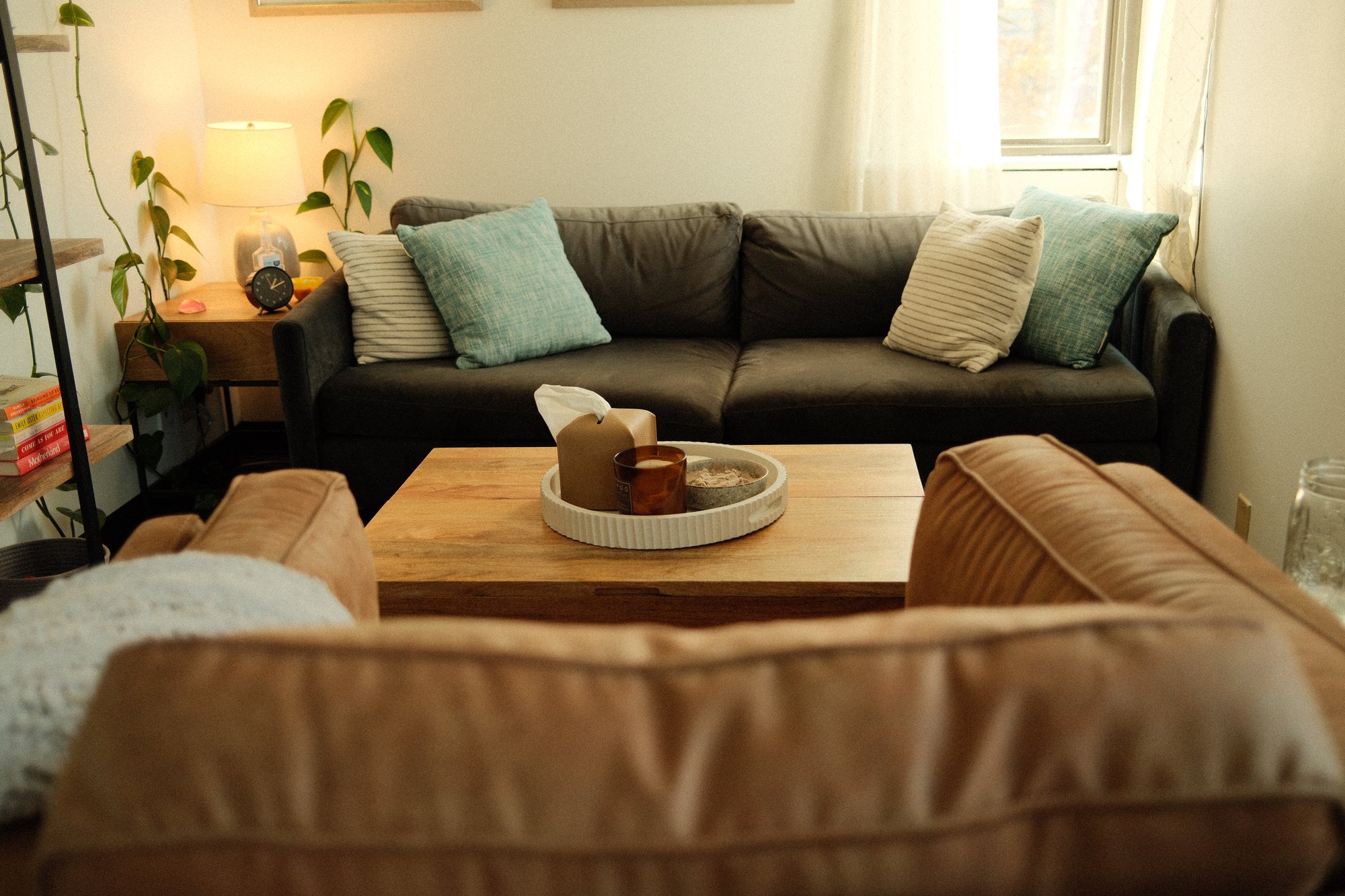 A view of the office sitting area, dark sofa with botanical prints above and a leather chair in the foreground.