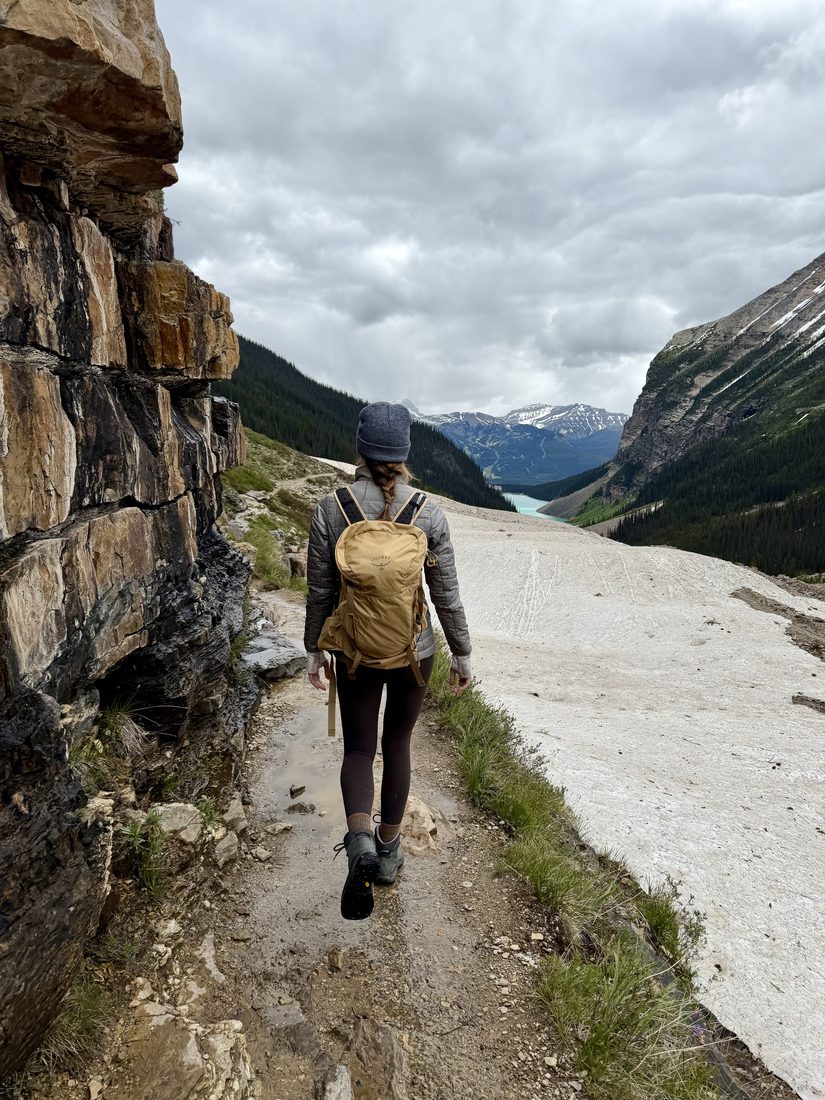 Cayce Smith hiking a mountain trail beside a turquoise lake.