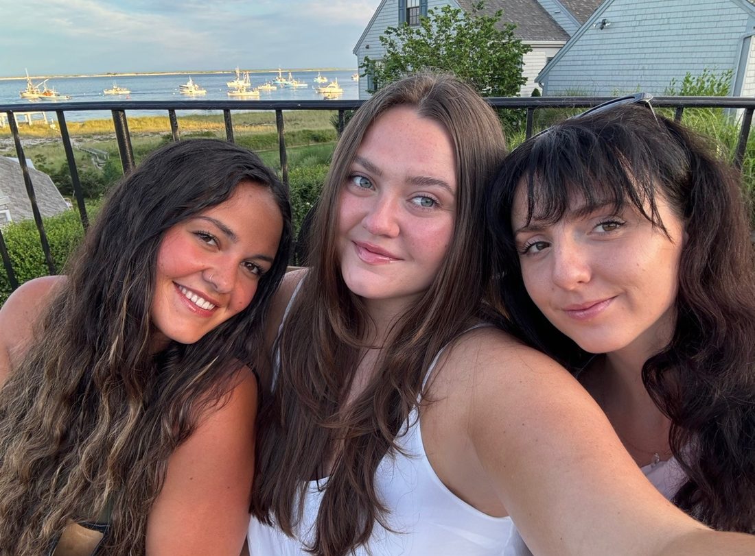 Elena Godbout with two friends on a deck overlooking a harbor at sunset.