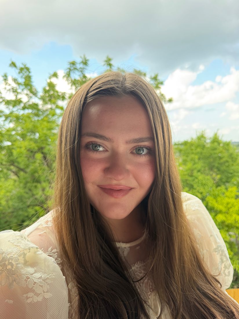 Elena Godbout smiling outdoors with trees and blue sky behind her.