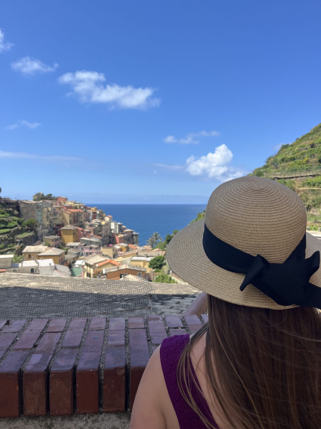 Jillee Walter looking out over a coastal Italian village, wearing a sun hat.