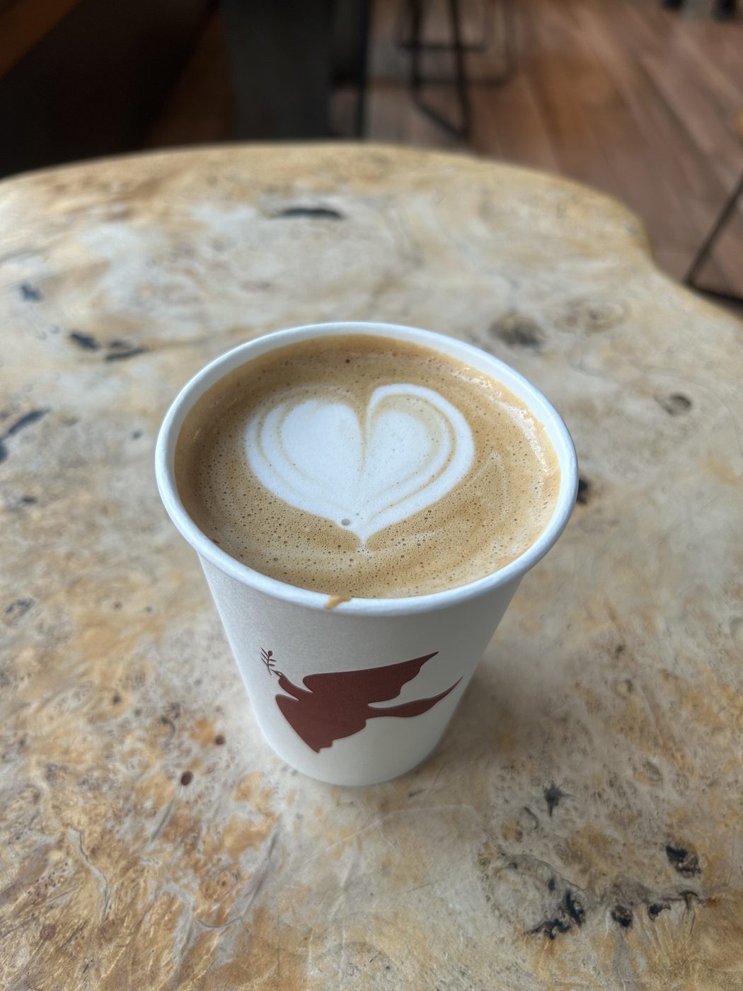 A latte with heart-shaped foam art in a paper cup on a wooden table.