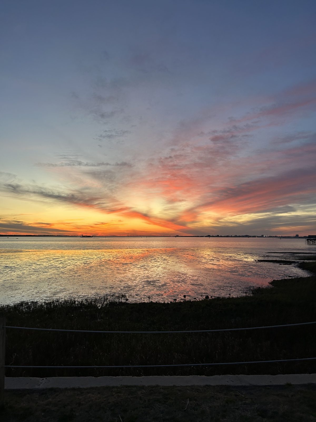 A pink and orange sunset reflecting over calm coastal water.